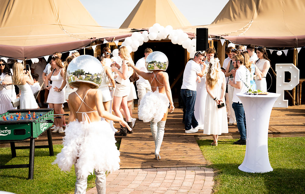 Women in white walking towards tipi with disco helmets.