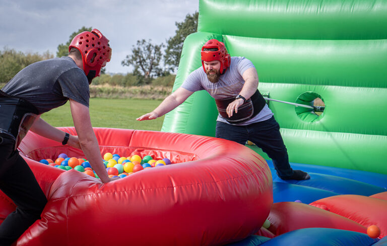 Two men on an inflatable grabbing colourful balls attached to a bungee
